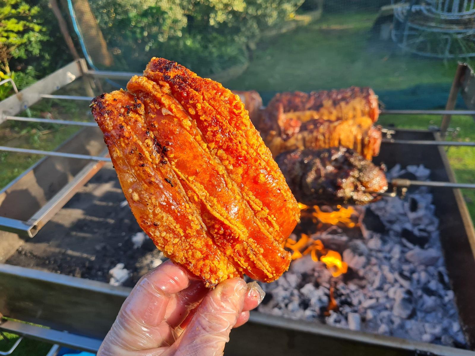 A strip of golden crackling held up over the coals