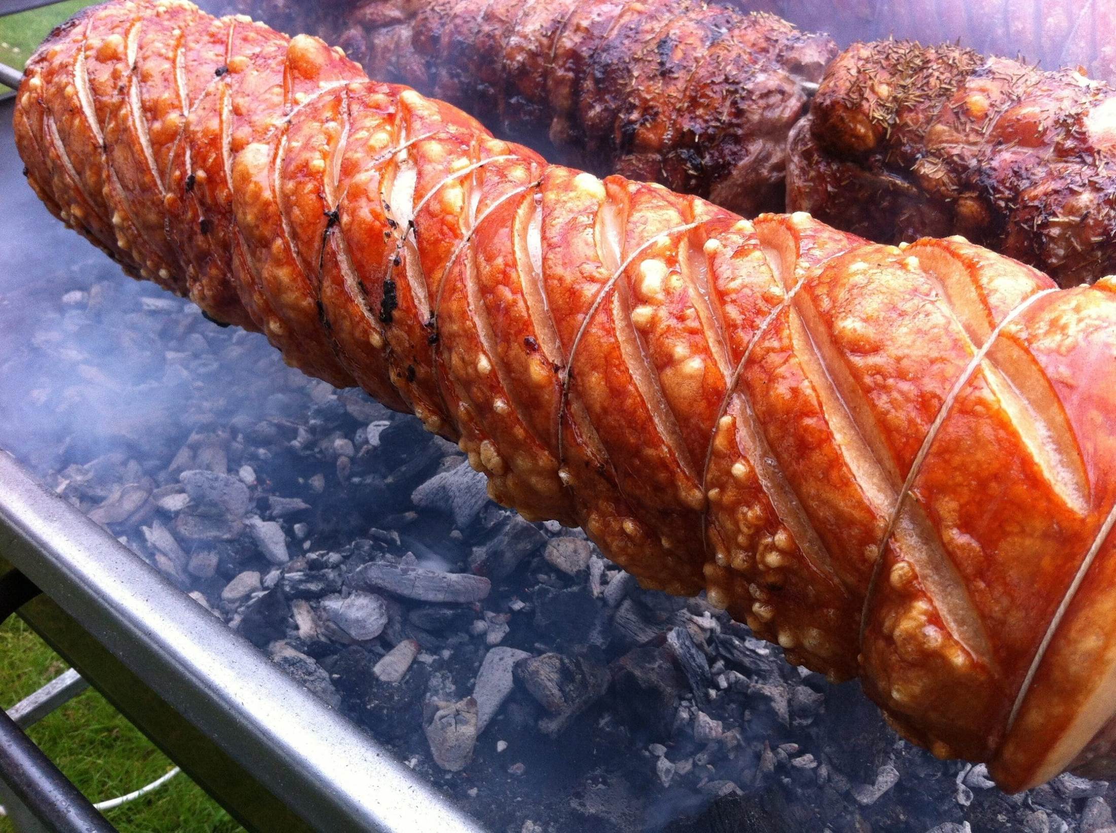Scored free-range pork loin turning on a spit over glowing charcoal