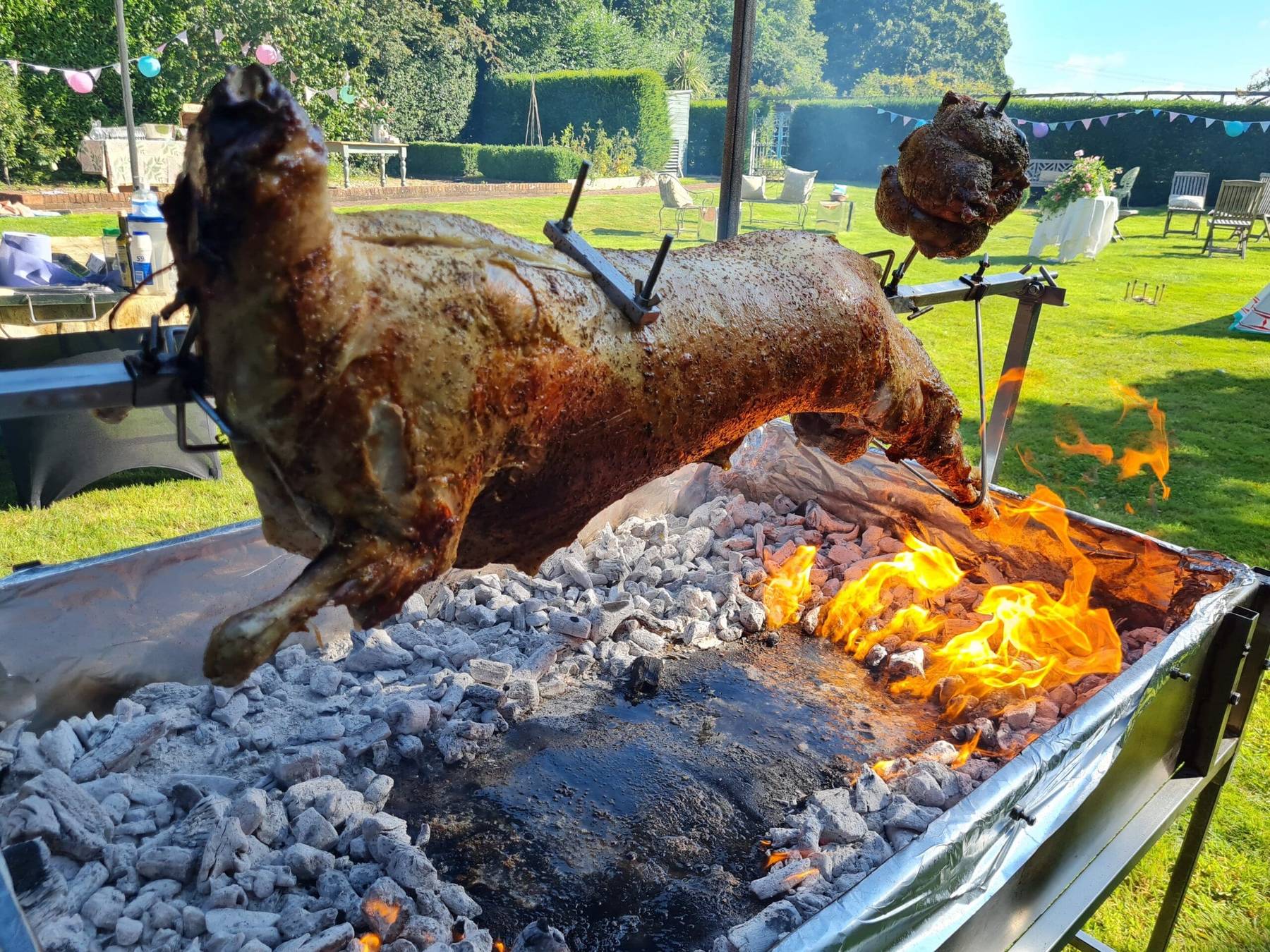 Lamb roasting over charcoal on a lawn decorated with bunting