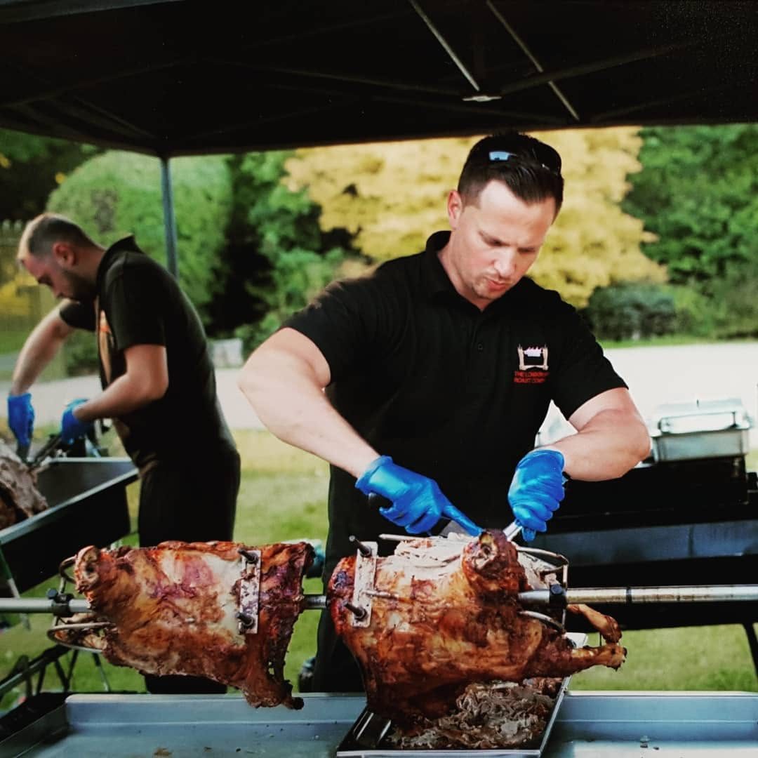 Chef carving two charcoal-roasted suckling pigs on the spit