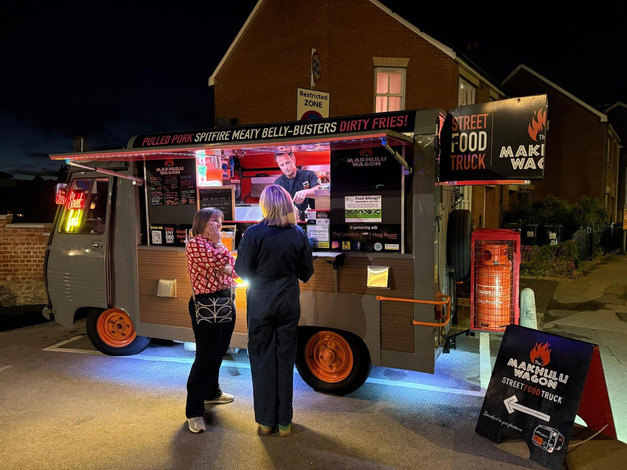 The Makhulu Wagon food truck lit up at night with customers at the hatch